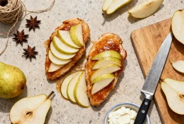 Filets de poulet nappés de glaçage avec écailles de poire disposées en motif, accompagnés de badiane et ingrédients sur plan de travail