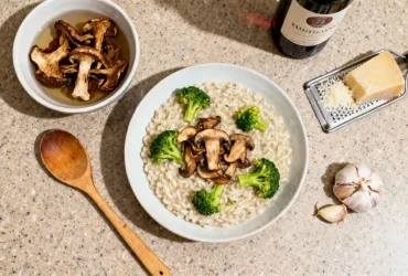 Risotto crémeux aux cèpes avec brocoli et parmesan sur plan de travail de cuisine, accompagné d'ingrédients comme ail et vin de cuisson